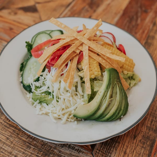 A vibrant Mexican salad with tortilla strips, corn, avocado, cheese, and fresh vegetables on a white plate.