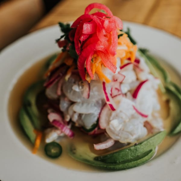 Mexican ceviche with shrimp, red onion, avocado, and chili peppers on a white plate.